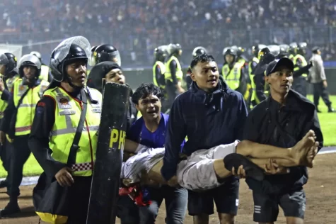 Fans attempt to carry injured fan off of the field where stampede broke out in Indonesia at Kanjuruhan Stadium. 