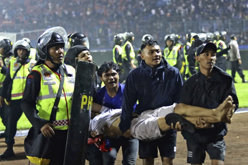 Fans+attempt+to+carry+injured+fan+off+of+the+field+where+stampede+broke+out+in+Indonesia+at+Kanjuruhan+Stadium.+