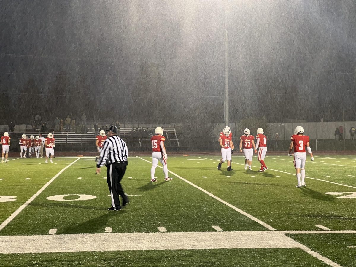 The Knights huddle up under the Friday night lights and a torrential downpour. Photo by Elliotte Banziger.